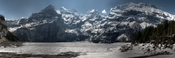 Zugefrorener Oeschinensee im Winter, umgeben von schneebedeckten Bergen